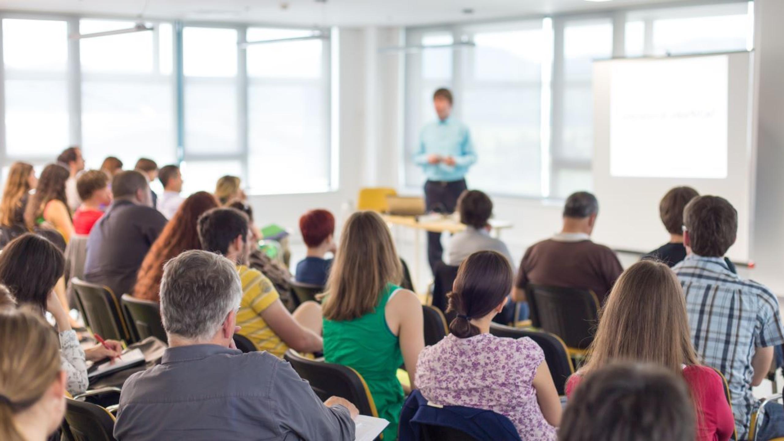 Groep mensen volgt les in witte zaal.